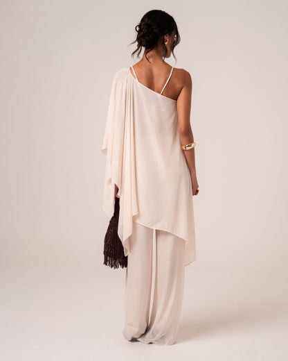 Back view of a sheer ivory viscose resort cape worn one-shoulder with white wide-leg pants — luxury resortwear