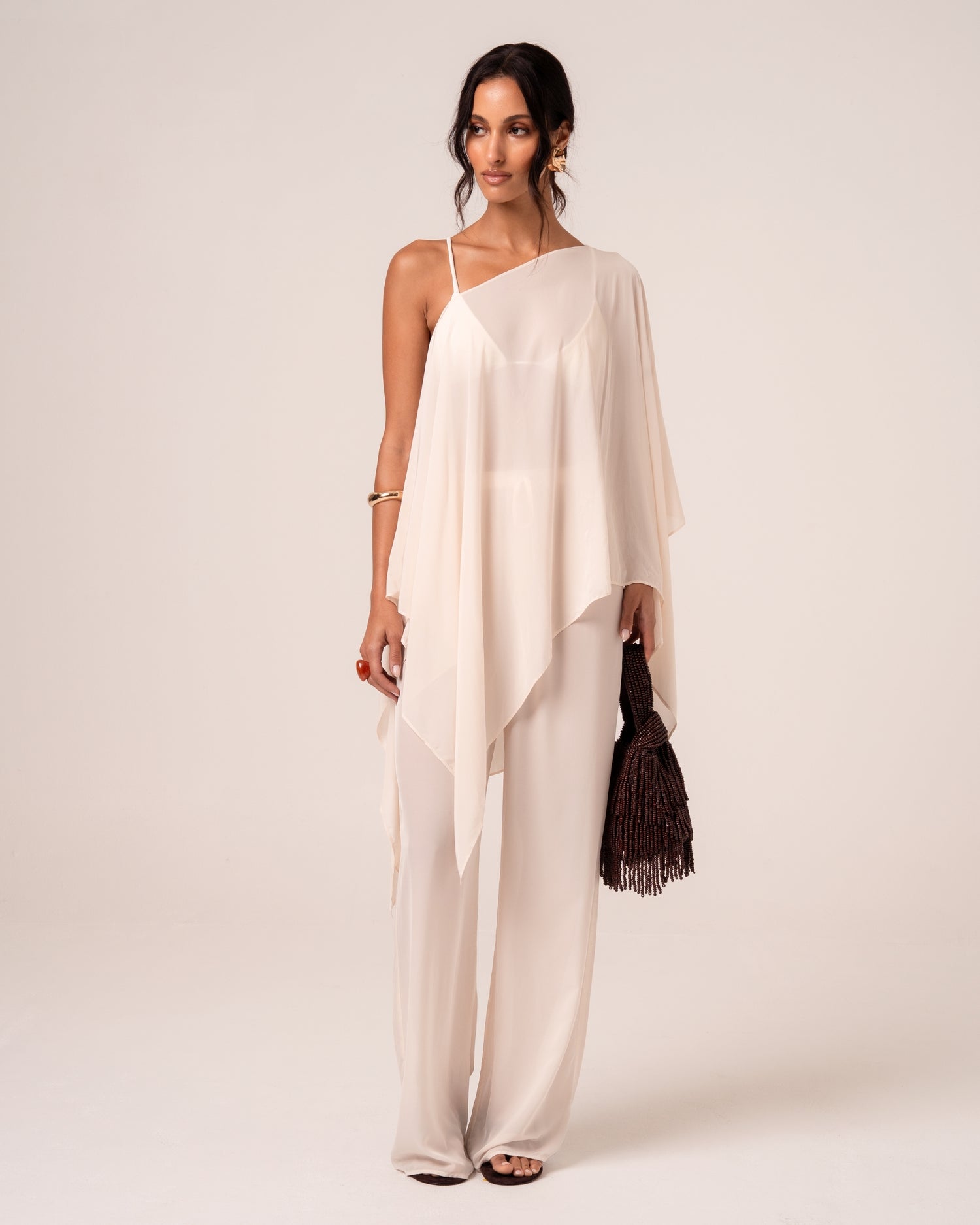 Ivory resort cape draped one-shoulder over wide-leg pants — versatile bridal resortwear for honeymoon evenings