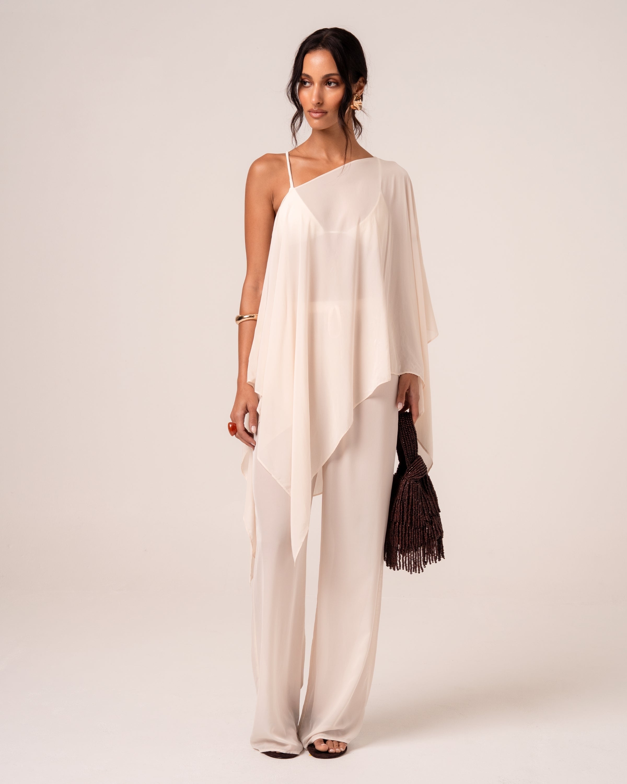 Ivory resort cape draped one-shoulder over wide-leg pants — versatile bridal resortwear for honeymoon evenings