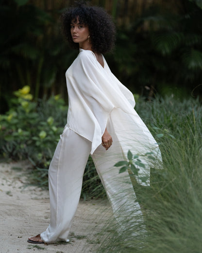 Side view of a sheer ivory resort cape layered over white palazzo pants in a tropical garden — elegant honeymoon resortwear