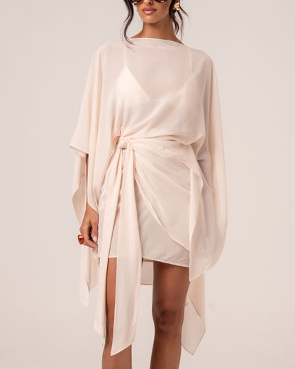 Close view of an ivory sarong-style wrap mini skirt showing the self-tie knot at the hip and curved wrap hem