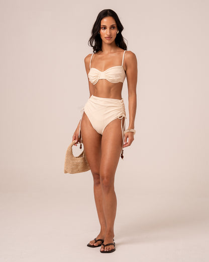 Model wearing an ivory soft cup bralette bikini top with ruched centre gathering, styled with a high waist bottom — studio front view