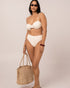 Ivory mid rise bikini bottom shown at the hip, the elongating spliced seams and higher leg foregrounded on a size 12 fit — studio side view