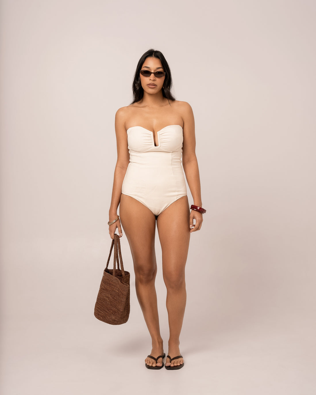Model wearing an ivory strapless bandeau one piece swimsuit with a V-wire plunge neckline, studio front view