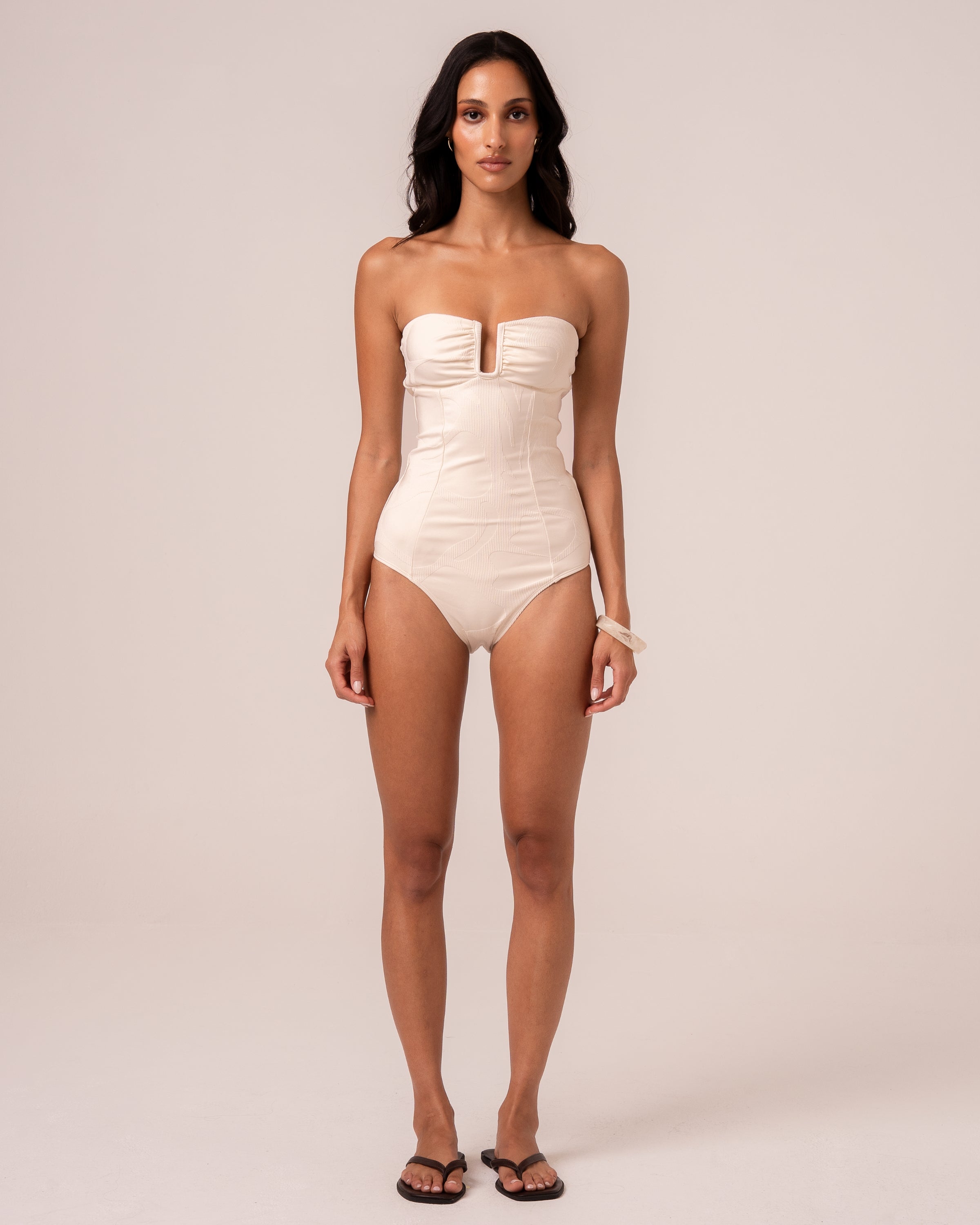 Model wearing an ivory strapless bandeau one piece swimsuit with a V-wire plunge neckline and sculpting seams, studio front view