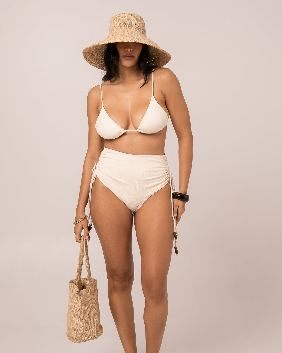 Model wears the ivory string triangle bikini top with thin adjustable straps and jacquard rib texture, front studio view.