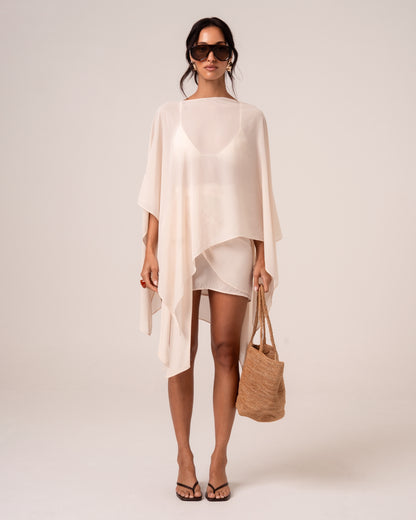 Model wearing a sheer ivory viscose resort cape over a matching bikini and mini skirt — elevated honeymoon resortwear, front view
