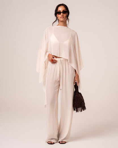 Model wearing ivory wide-leg resort pants with an elasticated drawstring waist and a matching sheer cape, front view