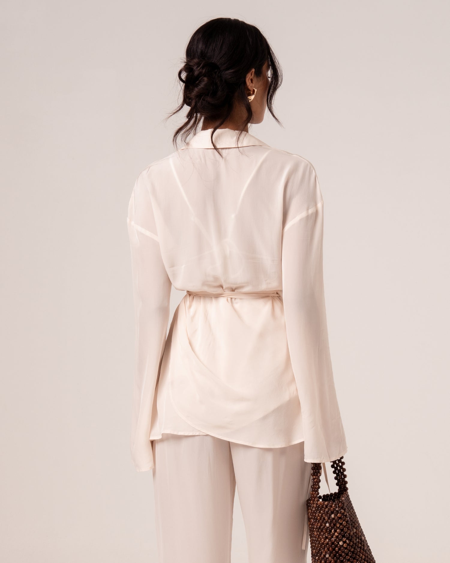 Back view of an ivory viscose wrap shirt with relaxed collar and wraparound waist tie, worn over wide-leg resort pants