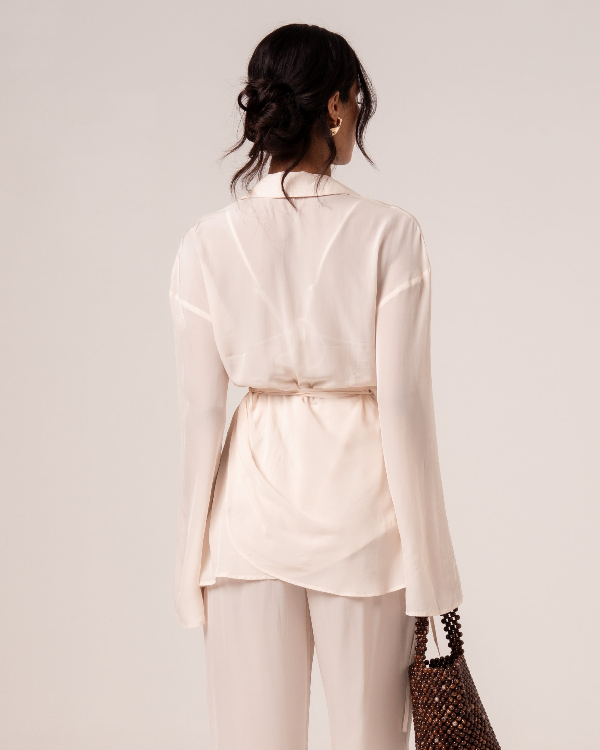 Back view of an ivory viscose wrap shirt with relaxed collar and wraparound waist tie, worn over wide-leg resort pants