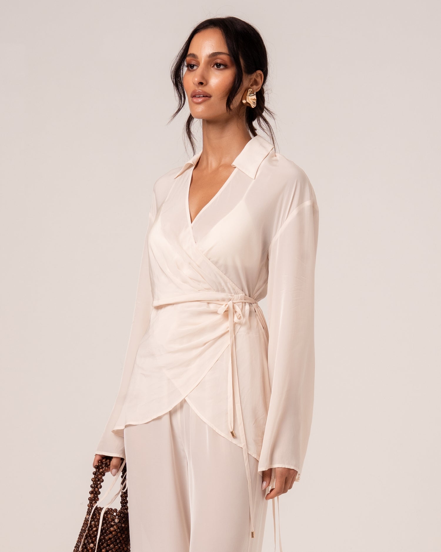 Close view of an ivory wrap shirt showing the V-neckline, relaxed collar and self-tie waist with gold-tipped ties