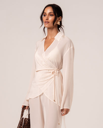 Close view of an ivory wrap shirt showing the V-neckline, relaxed collar and self-tie waist with gold-tipped ties
