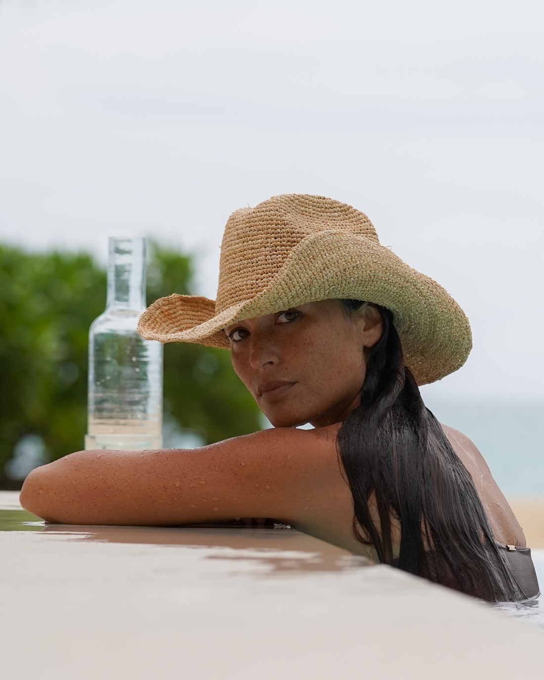 Close-up of a natural handwoven raffia cowboy hat with a shaped wide brim, worn poolside at a beach resort