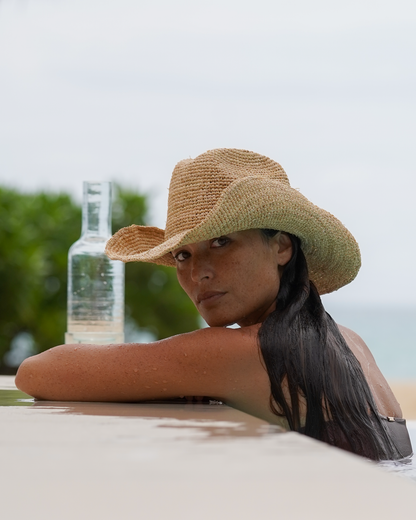 Close-up of a natural handwoven raffia cowboy hat with a shaped wide brim, worn poolside at a beach resort