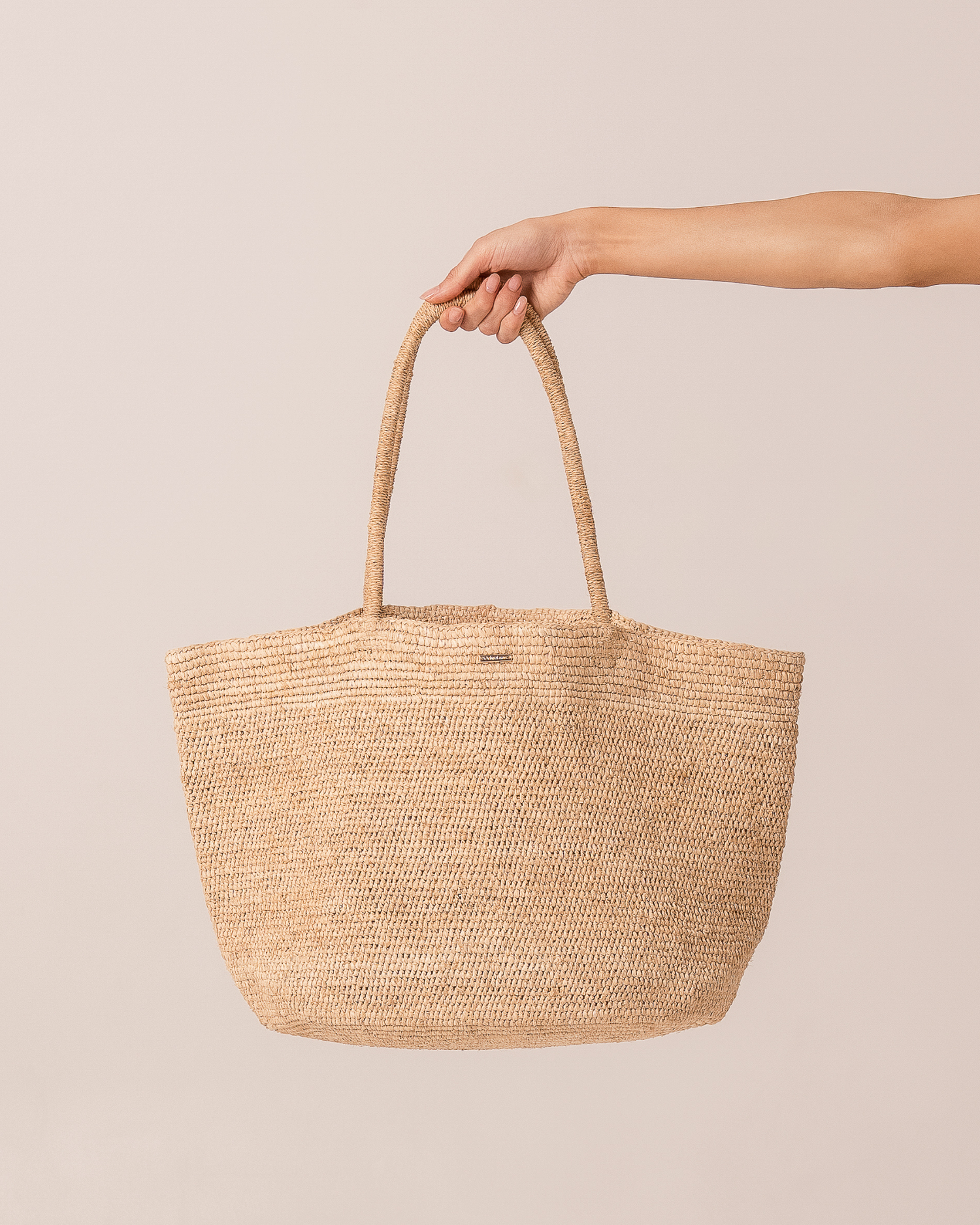 Natural raffia straw maxi tote bag held by the handle, front product view on a plain neutral background