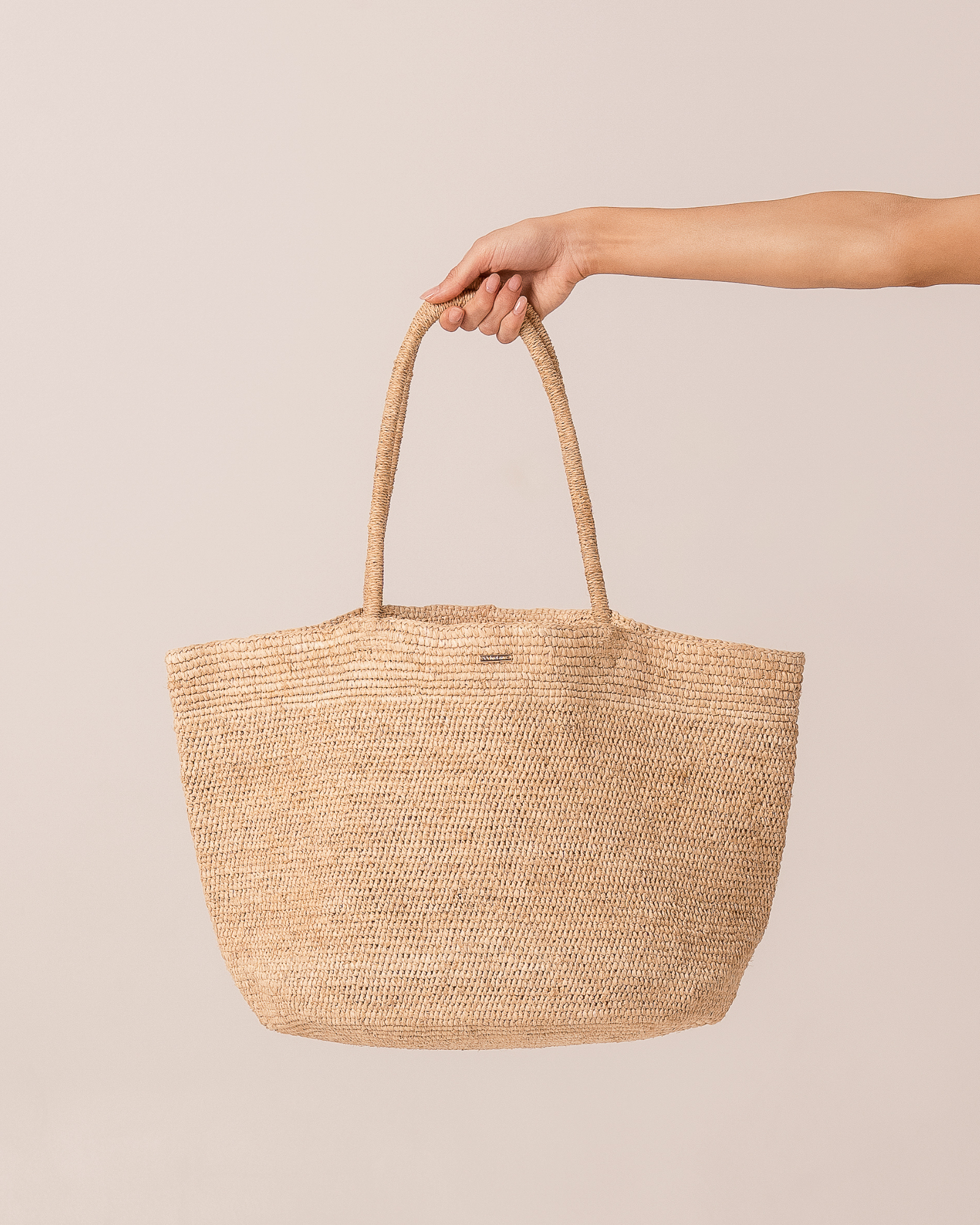 Natural raffia straw maxi tote bag held by the handle, front product view on a plain neutral background