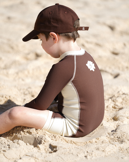Children’s brown surfsuit with contrast cream detailing photographed at the shoreline