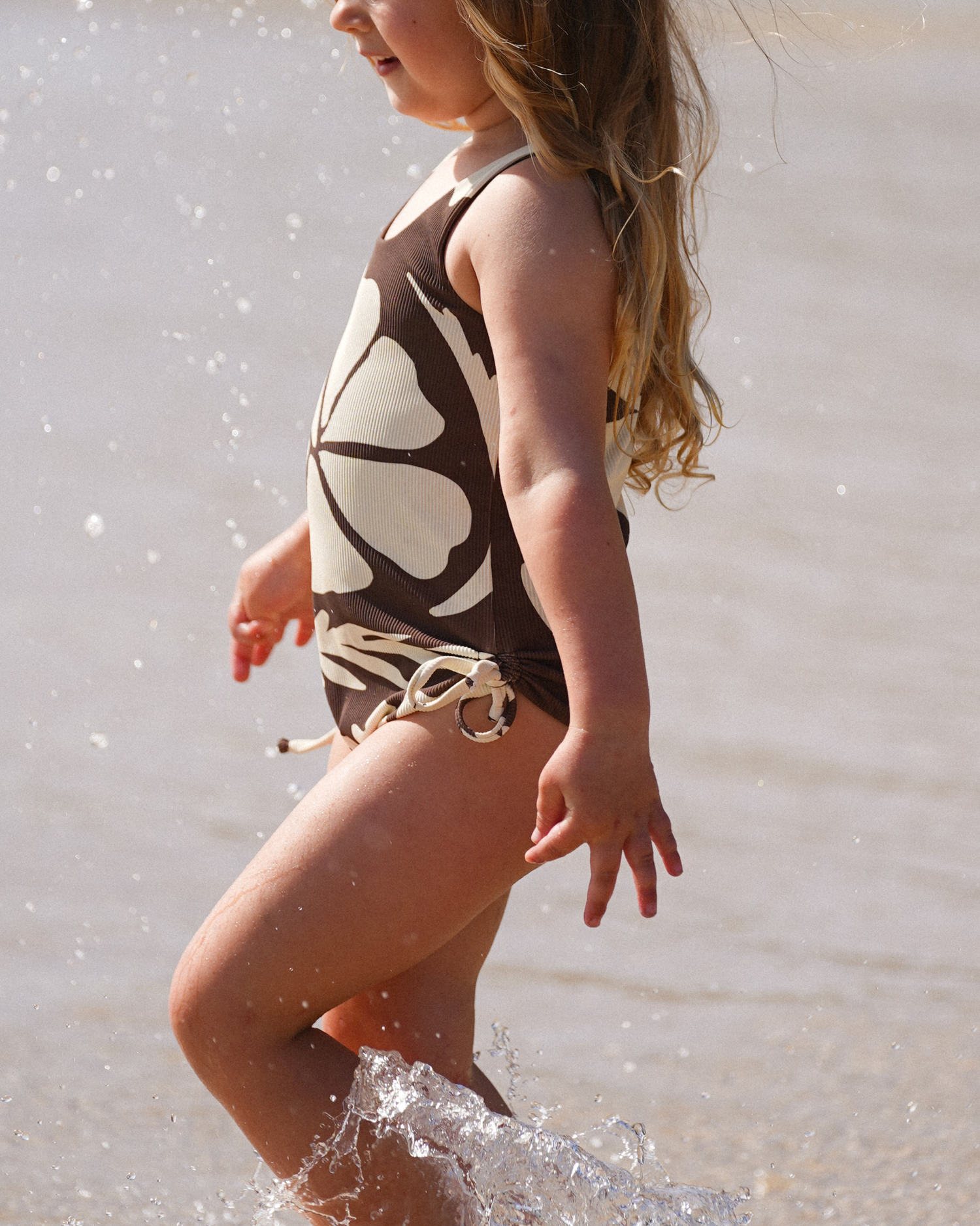 Girl wearing Ochre Lane Ibisco kids scoop one piece in brown floral print at the beach