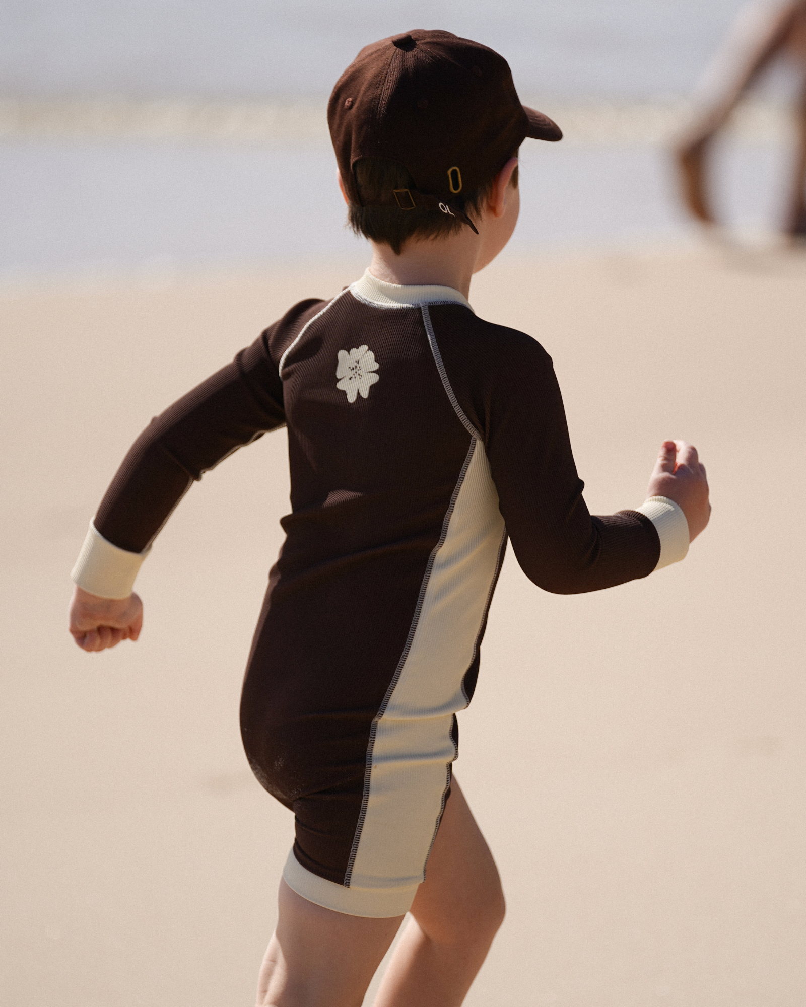 Boy wearing Ochre Lane kids chocolate surfsuit with cream contrast panels on the beach