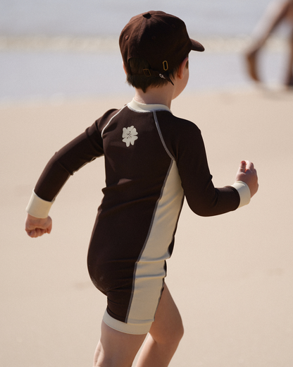 Boy wearing Ochre Lane kids chocolate surfsuit with cream contrast panels on the beach
