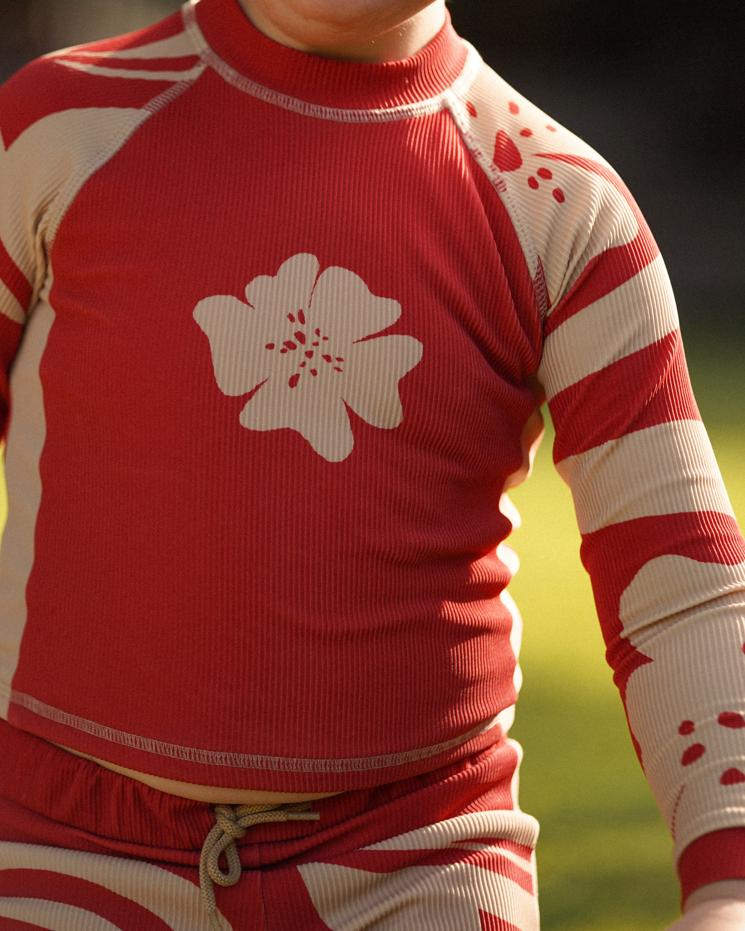 Child wearing Ochre Lane kids long sleeve red floral Solana rash shirt under outdoor shower