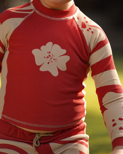 Child wearing Ochre Lane kids long sleeve red floral Solana rash shirt under outdoor shower