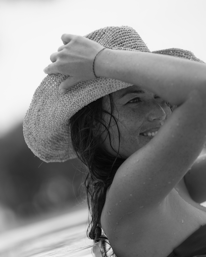Detail of the handwoven raffia weave and wide brim of a natural straw cowboy hat, held by a smiling model
