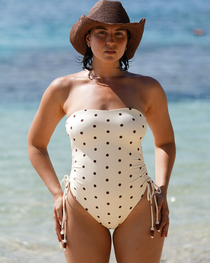 Ochre Lane polka dot one piece swimsuit in Butter Dot, styled with side ruching and a clean strapless neckline, photographed seaside.