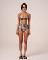 Model wearing zebra print high-waisted bikini bottoms with ruched side ties and wooden bead accents, paired with a matching bralette top, studio front view