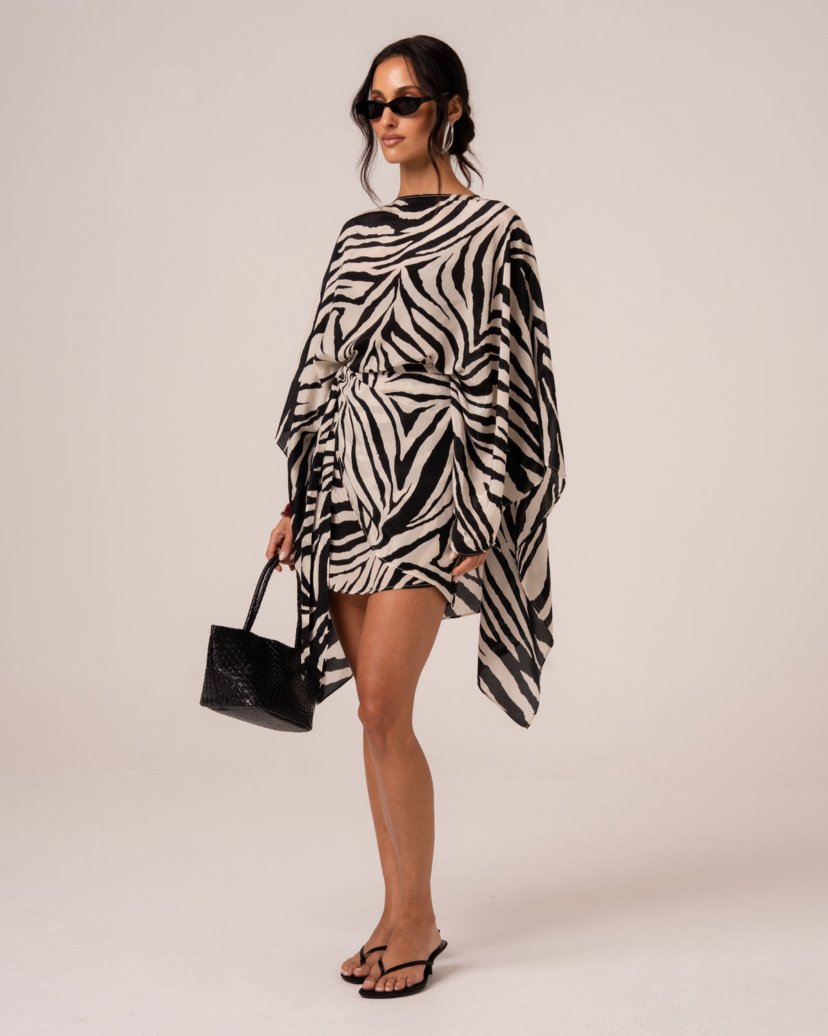 Front view of a zebra print sheer resort cape draped over one shoulder, styled with a woven tote