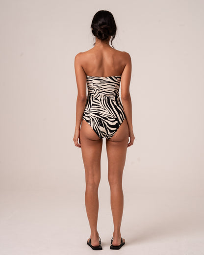 Back view of a zebra print bandeau one-piece with a cut-out waist strap, gold buckle closure, and high-cut leg