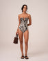 Model wearing a zebra print strapless bandeau one-piece with a notched V neckline and gold clasp, ruched side ties, styled with a beaded resin bucket bag, studio front view