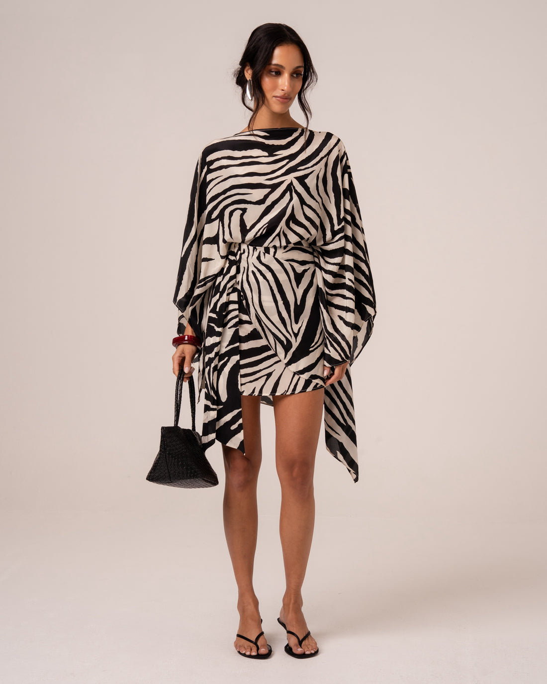 Model wearing a zebra print sheer resort cape with a clean bateau neckline, draped over a mini dress, studio front view